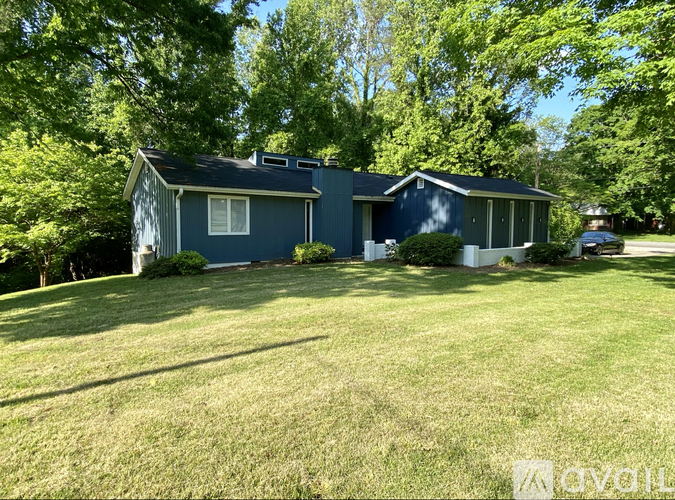 A blue house with a white window and a dark roof is surrounded by green trees.