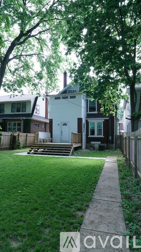 A house with a white exterior and a brown roof is surrounded by a fence and has a small garden in front.