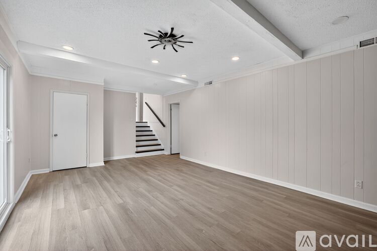 A spacious room with wooden flooring and a staircase in the background.