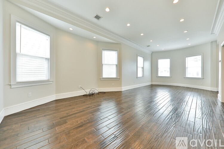 A spacious room with wooden flooring and windows on three walls.