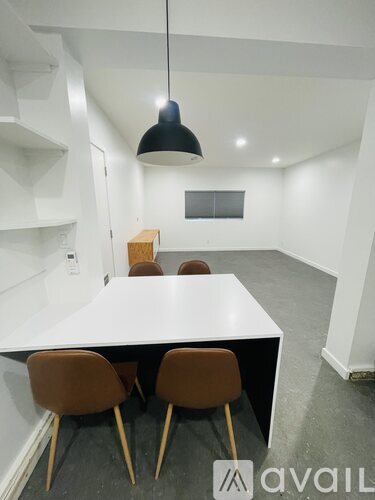 A white table with four chairs and a black pendant light hangs over it.