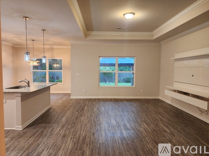 A spacious room with wooden flooring and a window overlooking a fence.