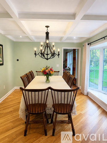 A dining room with a chandelier, a table with chairs and a vase of flowers.