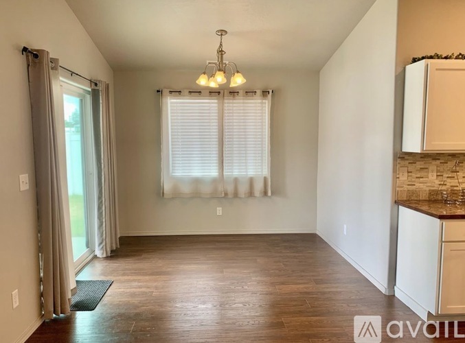 A room with a window covered by white blinds and a chandelier hanging from the ceiling.