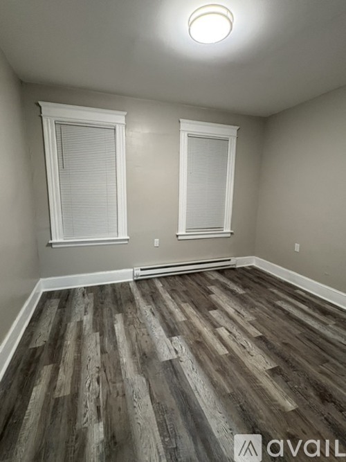 A room with wooden flooring and two windows.