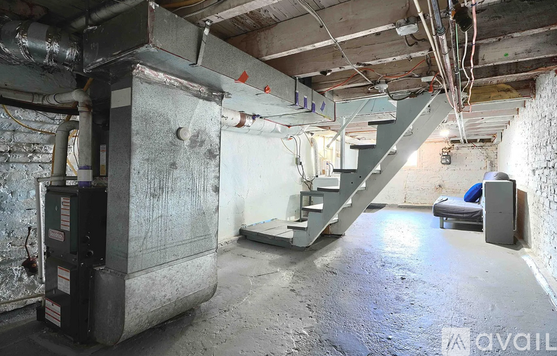 A dirty basement with a staircase and a furnace.