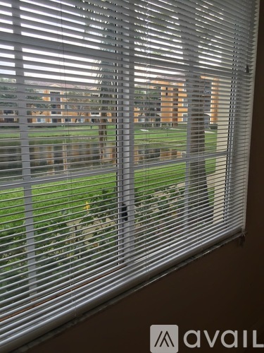 A window with blinds overlooking a grassy area.