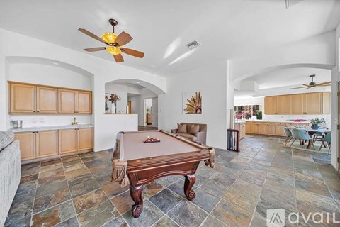 A pool table is in the middle of a room with a fan overhead.