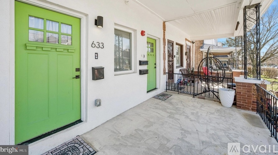 A bright green door is on the left side of a white house with the number 633 on it.