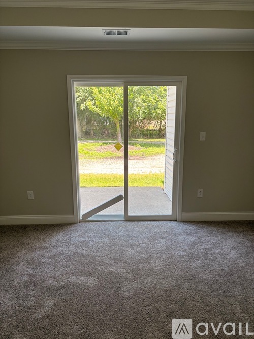 A room with a carpeted floor and a sliding glass door leading to a grassy area.