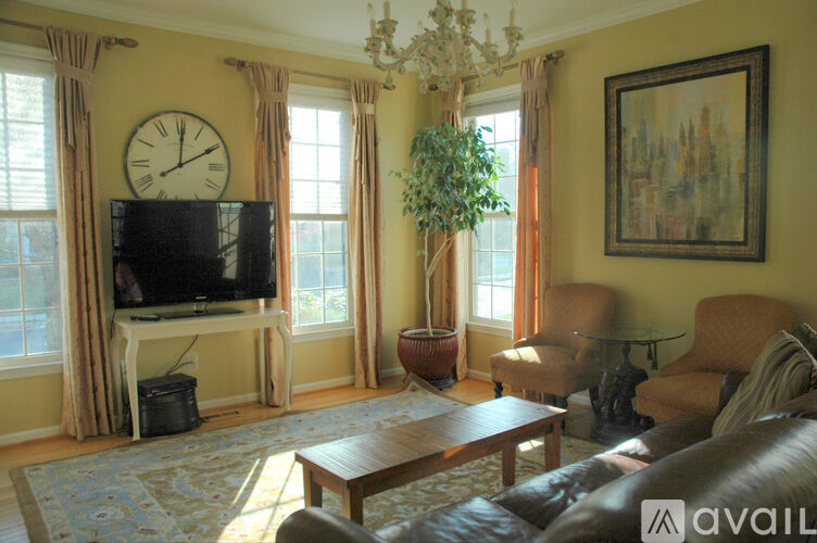 A living room with a television, a couch, a chair, a plant, and a painting on the wall.