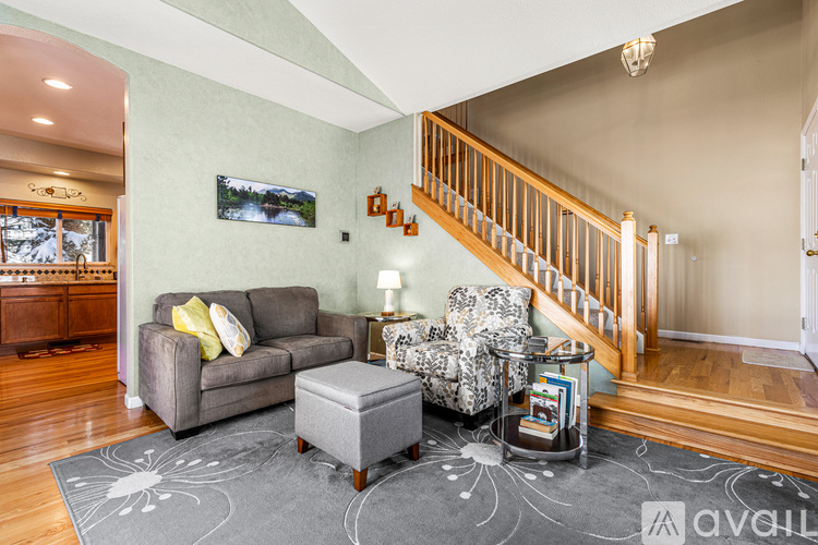 A living room with a grey couch, a grey ottoman, a chair with a floral pattern and a staircase.