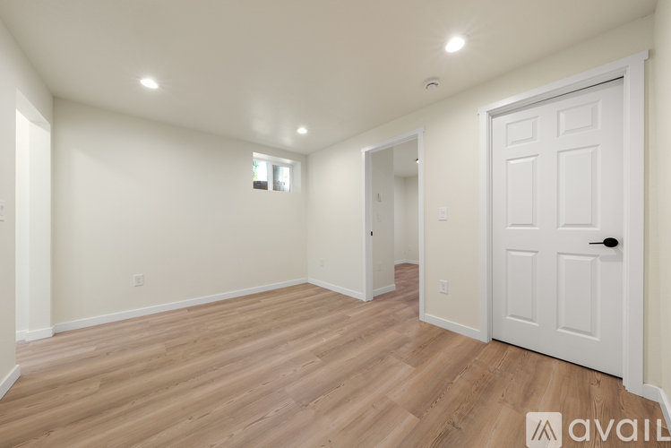 A room with wooden flooring and white walls, with a door on the right side.
