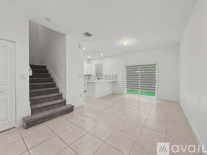 A spacious room with a staircase and a window with blinds.