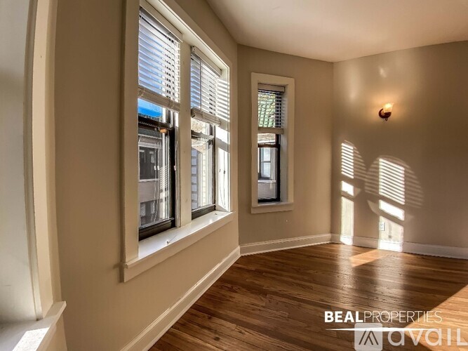 A room with wooden floors and two windows letting in sunlight.