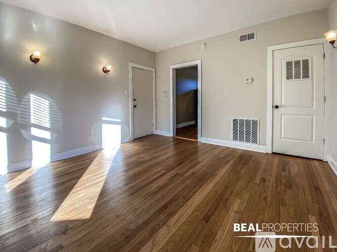 A room with wooden floors and white walls, with a door on the right and a window on the left.