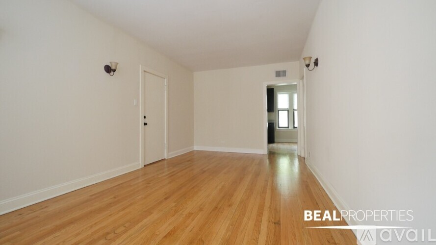 A room with wooden flooring and white walls, with a door and a window.