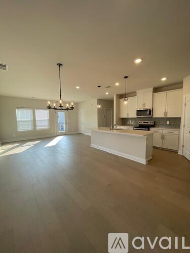 A spacious kitchen and living room with a chandelier and hardwood floors.