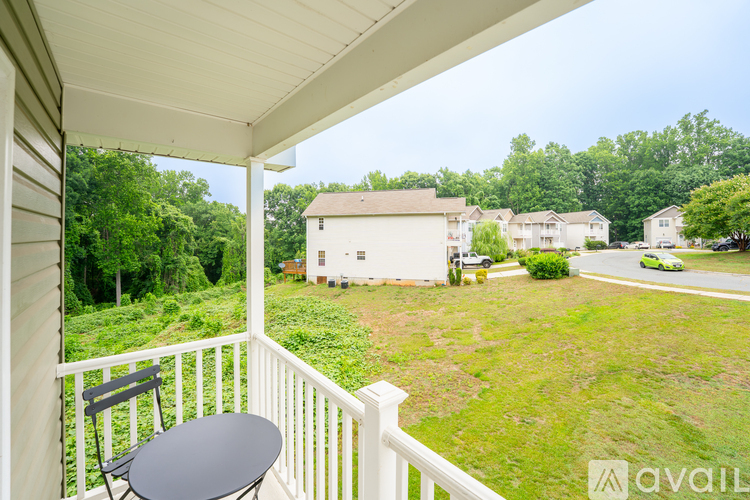 A balcony with a table and chairs overlooks a grassy area with houses in the distance.