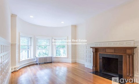 A large, empty room with a fireplace and a window overlooking a tree.