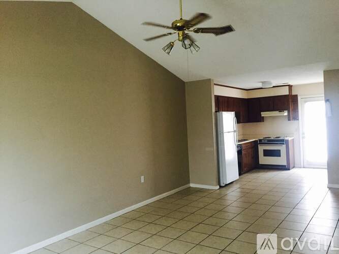 A room with a ceiling fan and a kitchen area in the background.