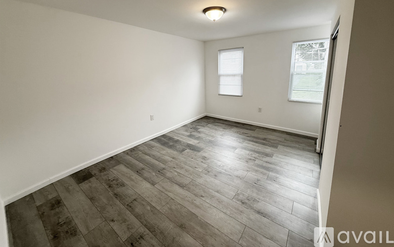 A spacious room with wooden flooring and two windows.