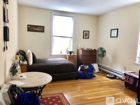 A room with a bed, a fan, and a table with a vase on it.