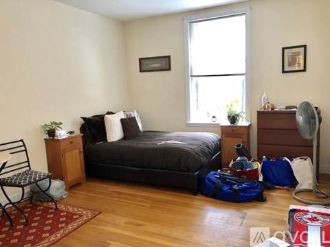 A bedroom with a bed, nightstand, chair, and luggage.
