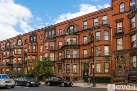 A row of brown buildings with cars parked in front.
