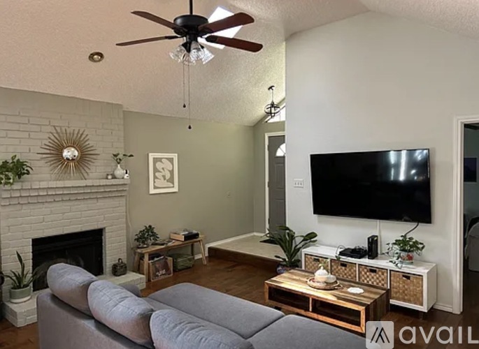 A living room with a grey couch, a fireplace, and a flat screen TV mounted on the wall.