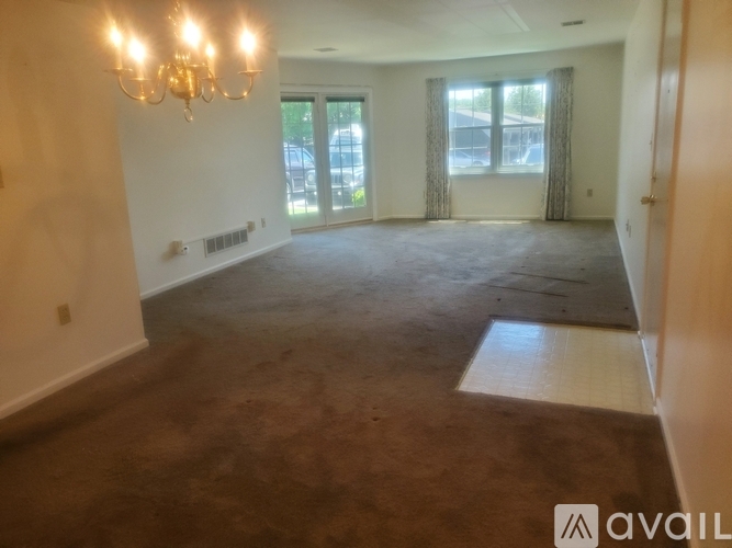 A room with a chandelier, carpeted floor, and a view of the outside through the window.