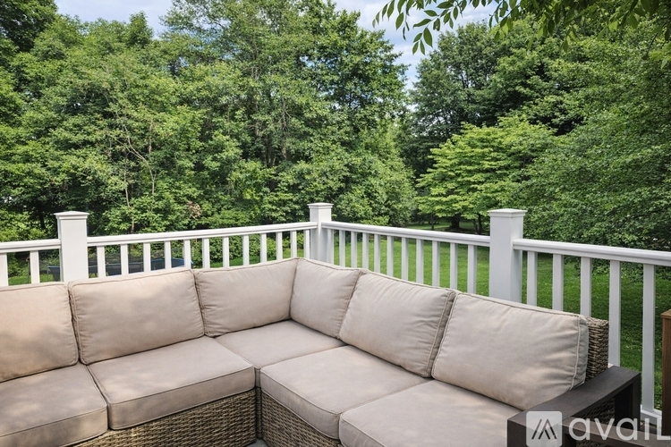 A white wicker sofa on a balcony with trees in the background.