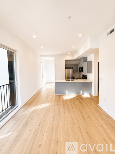 A spacious room with wooden flooring and a kitchen area in the background.