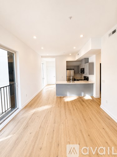 A spacious room with wooden flooring and a kitchen area in the background.