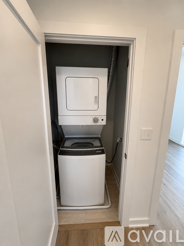 A small white washing machine is in a narrow space between two walls.