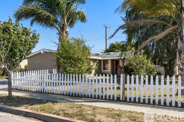 A white picket fence in front of a house with trees.