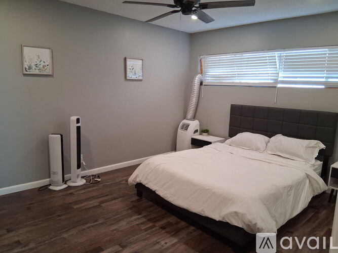 A bedroom with a bed, pillows, a fan, and a window with blinds.