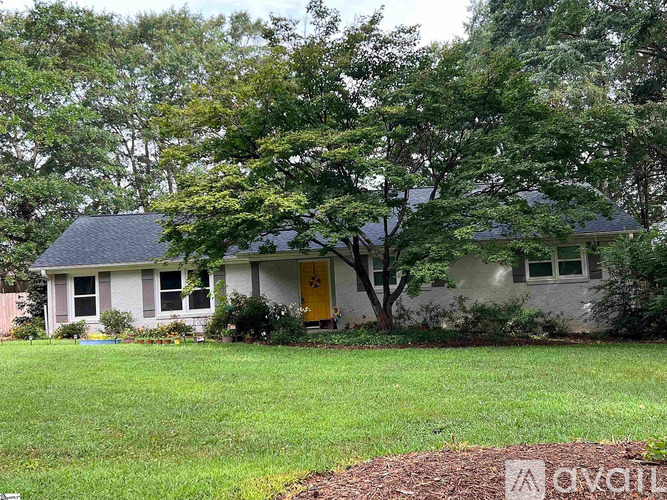 A house with a yellow door is surrounded by greenery.