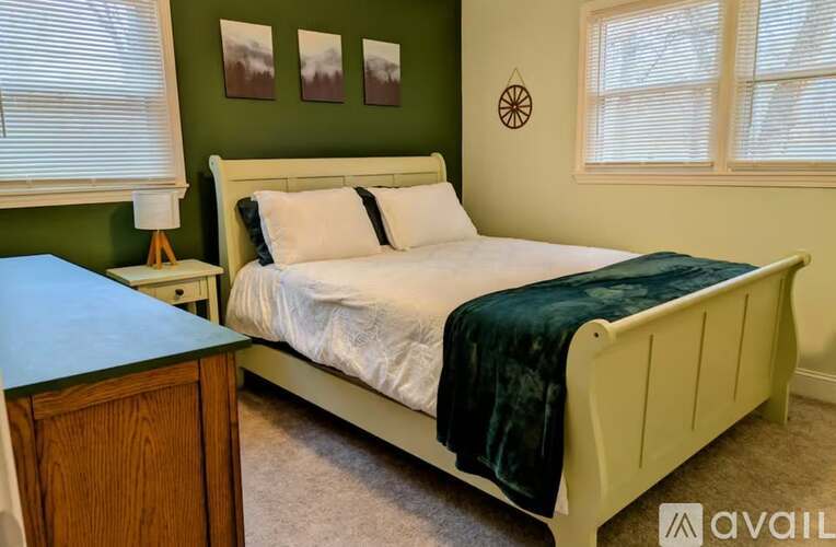 A bedroom with a white bed and green blanket.