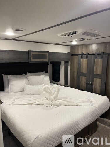 A bedroom with a bed, pillows, a towel folded into a heart shape, and a wooden headboard.