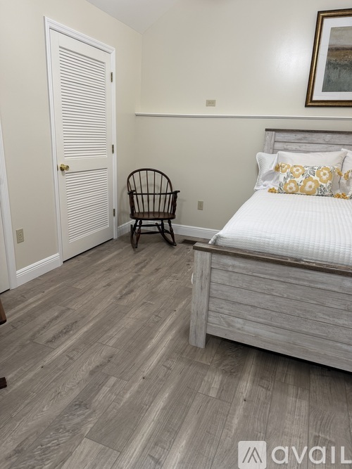A bedroom with a bed, chair, and wooden flooring.