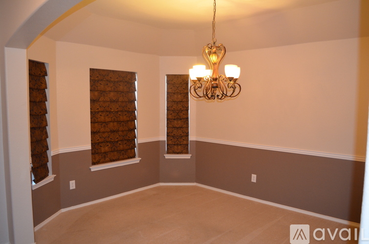 A room with a chandelier and two windows with brown blinds.