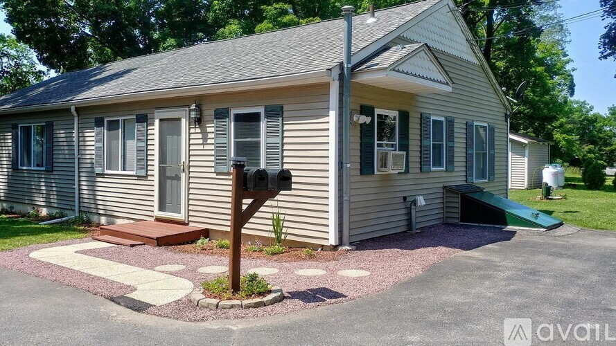 A house with a grey siding and a brown door is surrounded by a gravel driveway and a small garden.