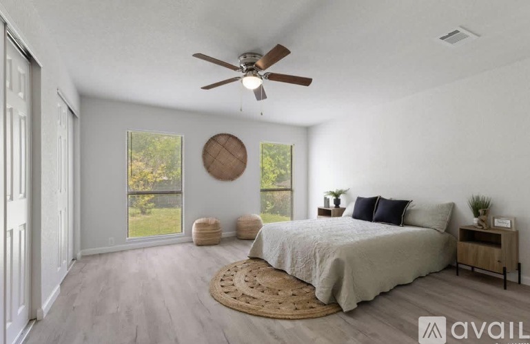 A bedroom with a bed, a ceiling fan, and a window with a view of trees.