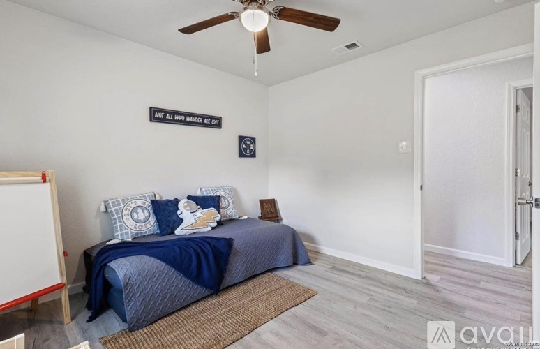 A bedroom with a blue bedspread and a ceiling fan.