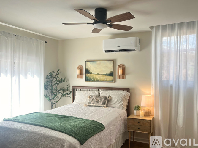 A bedroom with a bed, a ceiling fan, and a painting on the wall.