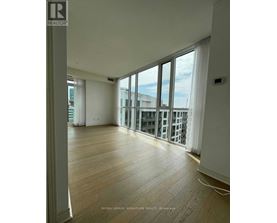 A spacious room with wooden flooring and large windows overlooking a cityscape.