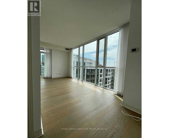 A spacious room with wooden flooring and large windows overlooking a cityscape.