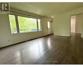 A room with wooden flooring and white walls, with a window on the left side.