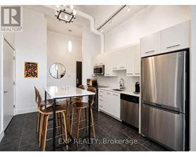 A modern kitchen with stainless steel appliances and wooden chairs.